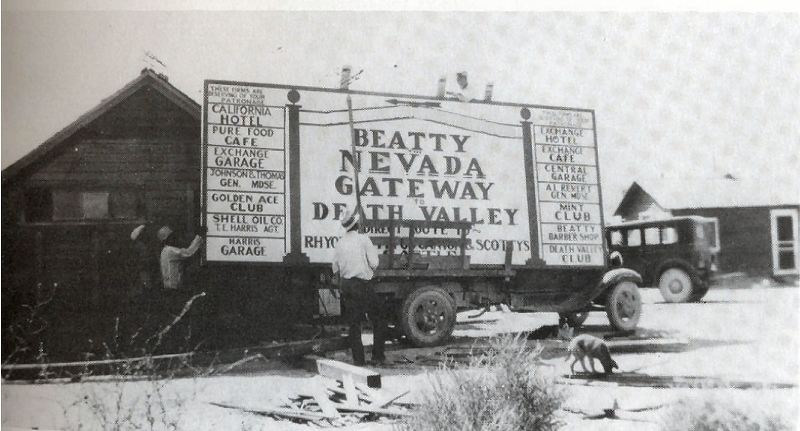 Men building a roadside billboard reading Beatty Nevada Gateway to Death Valley, listing the town's hotels, cafes and garages